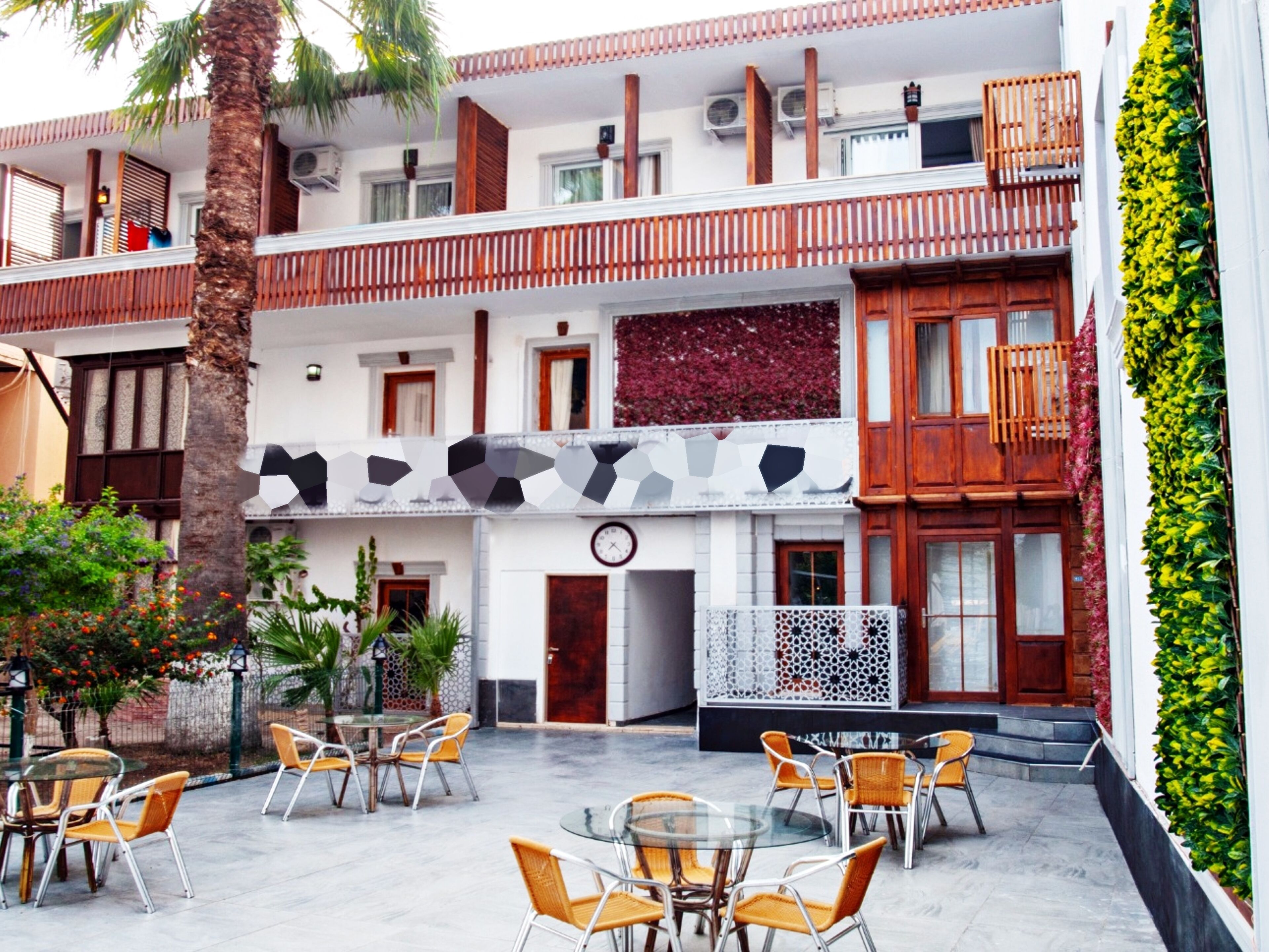 A two-story building with a balcony, outdoor seating area with chairs and tables, and a clock on the wall.