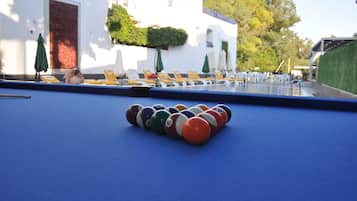 A pool table with numbered balls in front of a building with outdoor seating and umbrellas.