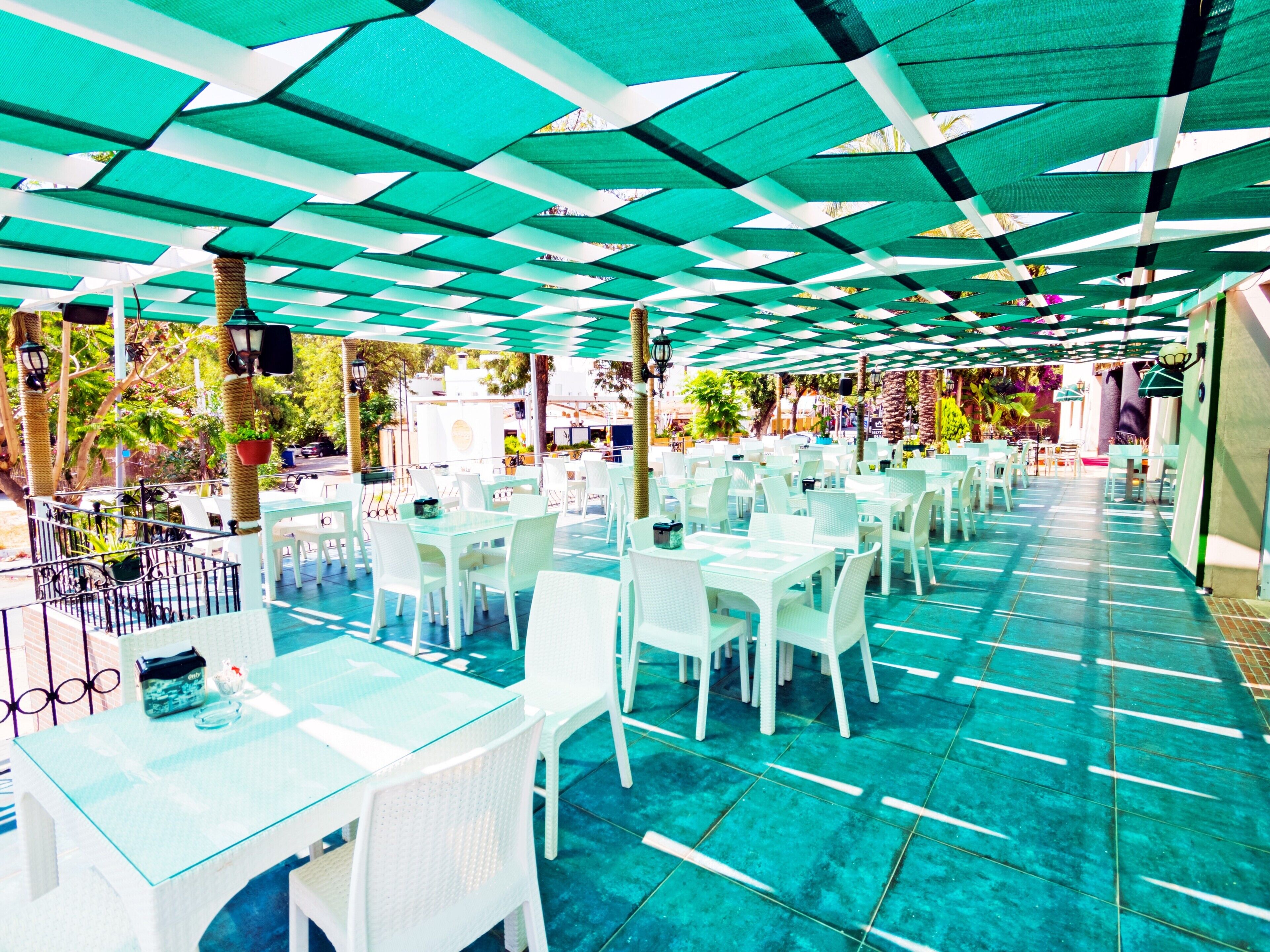 An outdoor dining area with white tables and chairs, a patterned ceiling, and a tiled floor.
