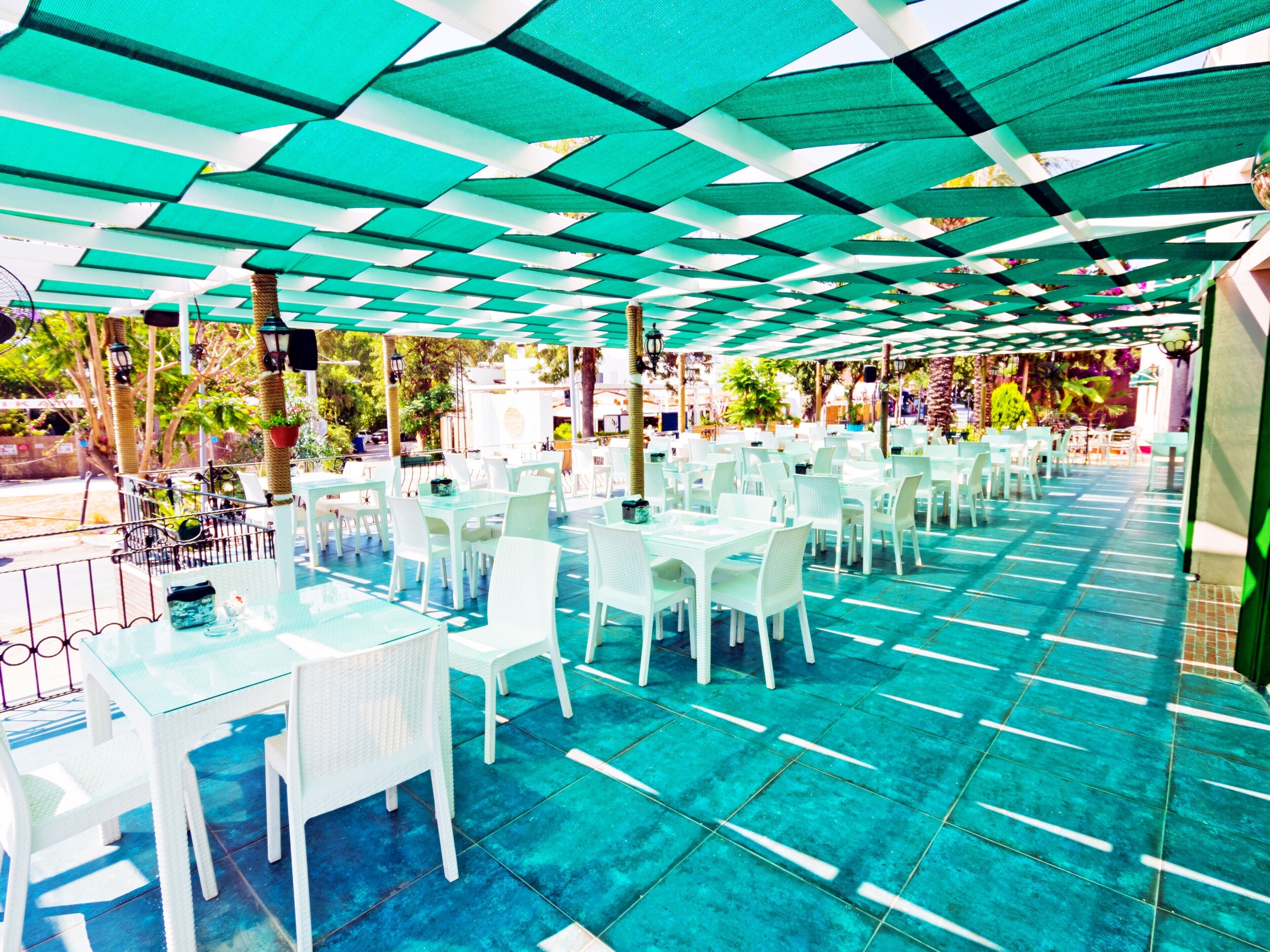 Un espace extérieur aménagé pour les repas, avec des tables et des chaises blanches, protégé par un auvent à motifs verts et blancs.
