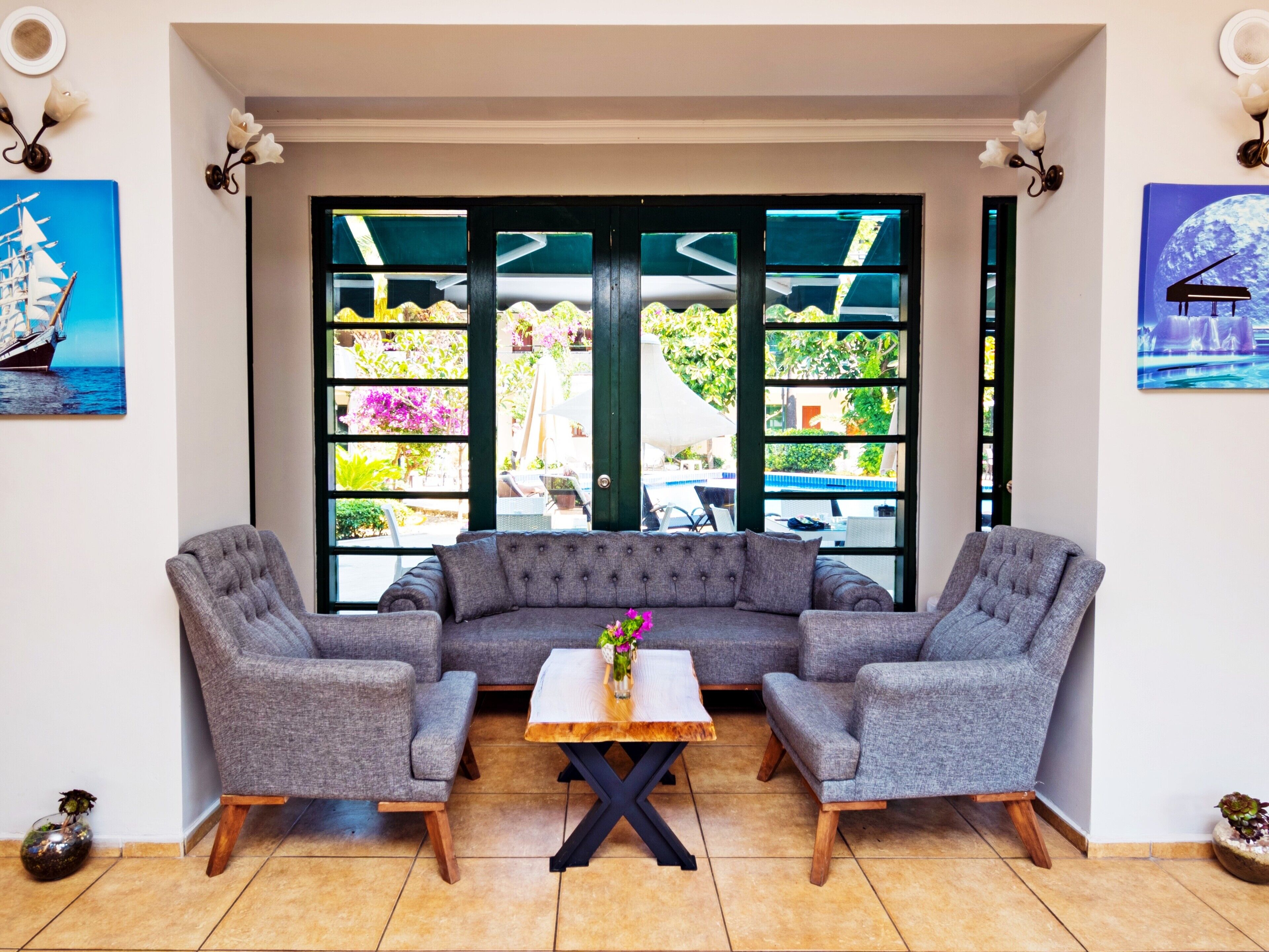 Een moderne woonkamer met een grijze modulaire bank, twee fauteuils, een houten salontafel en een uitzicht door grote ramen op een buitenste tuin.