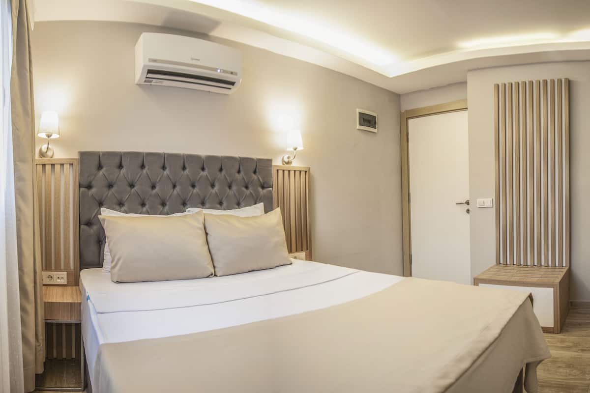 A hotel room with a large bed, bedside lamps, an air conditioner, a television, and a wooden desk.