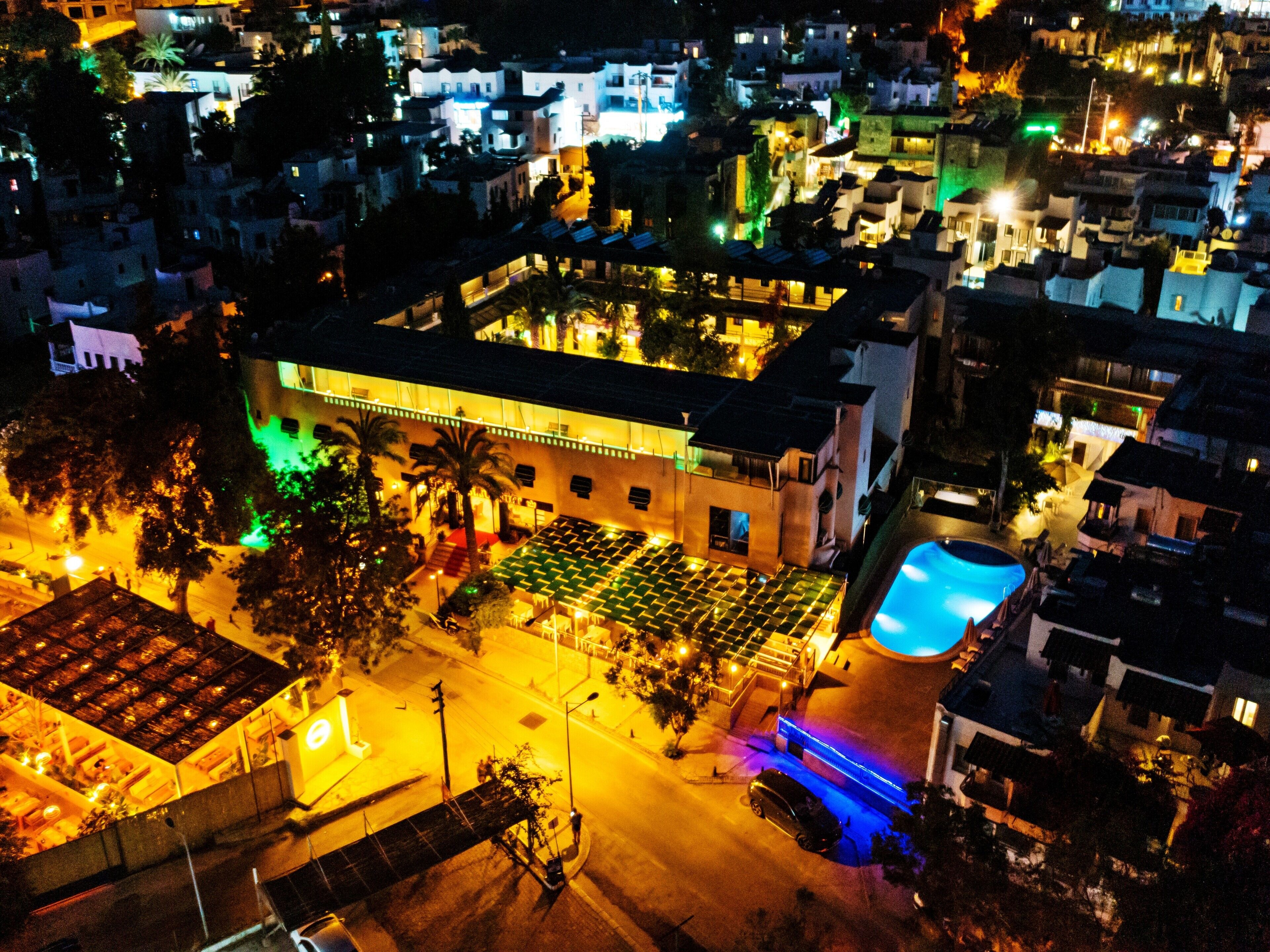 An aerial view of a hotel with a rooftop pool, multiple dining areas, and a street with parked cars.