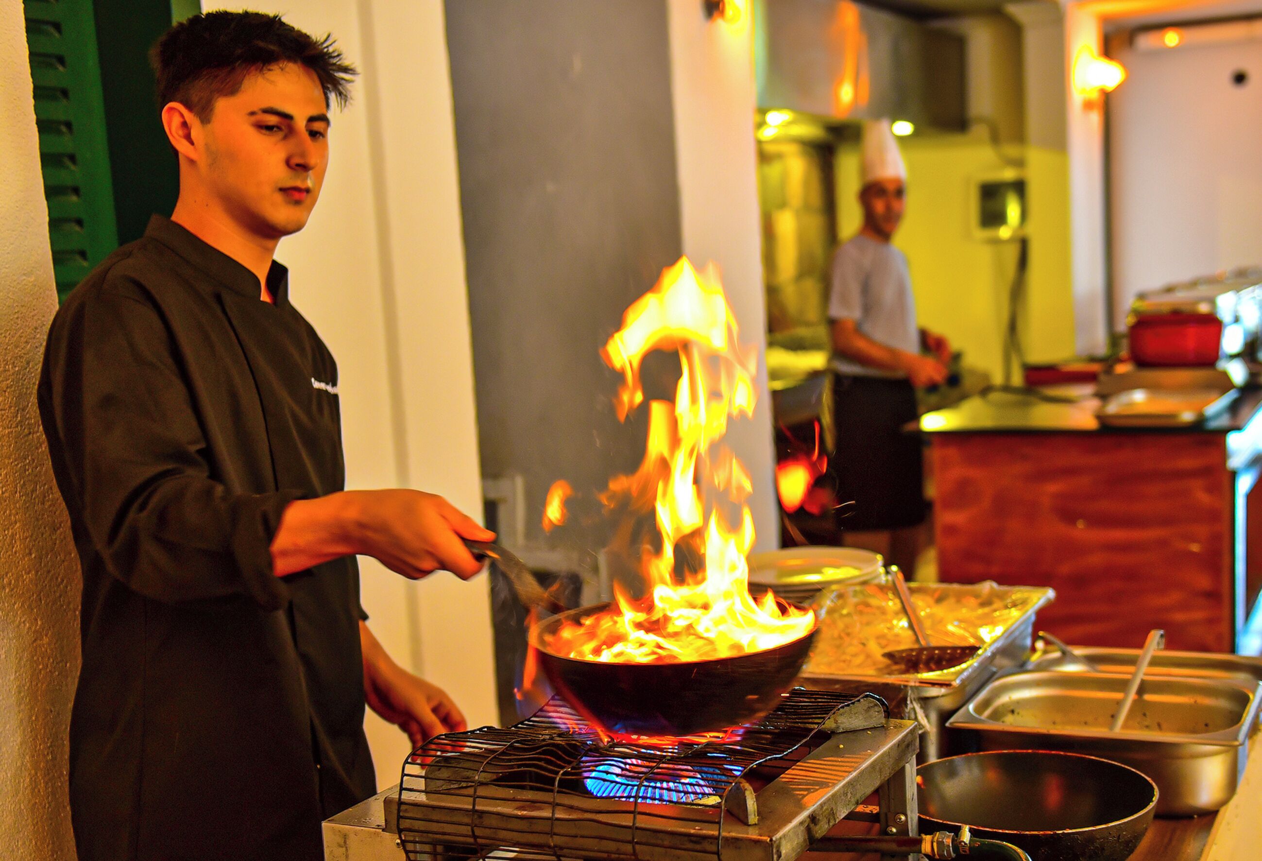 Ein Koch bereitet Essen mit einem brennenden Wok auf einem tragbaren Kochfeld zu.