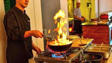 Ein Koch bereitet Essen mit einem brennenden Wok auf einem tragbaren Kochfeld zu.