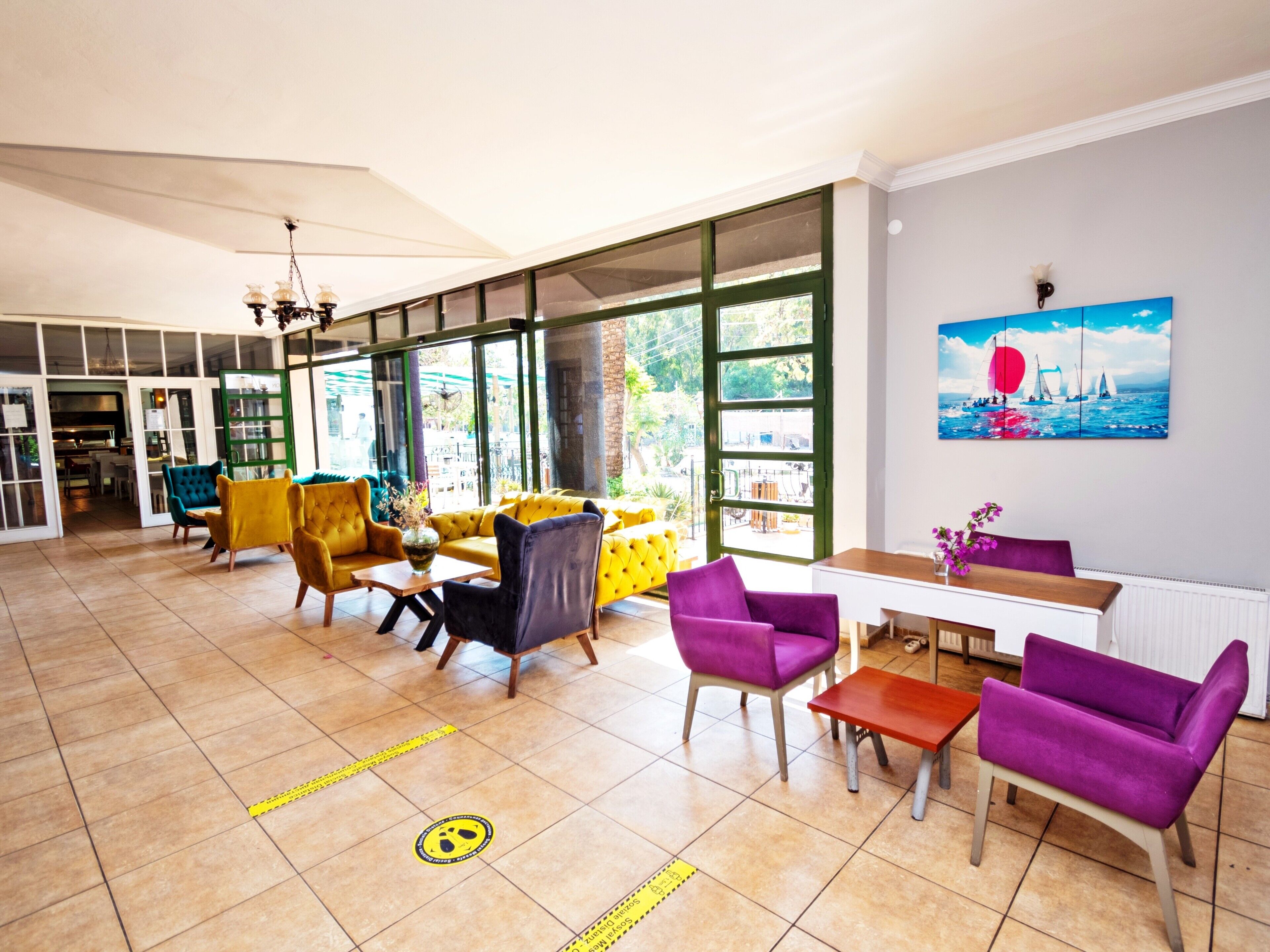 A spacious living area with a large window, yellow and purple chairs, and a table with a vase of flowers.