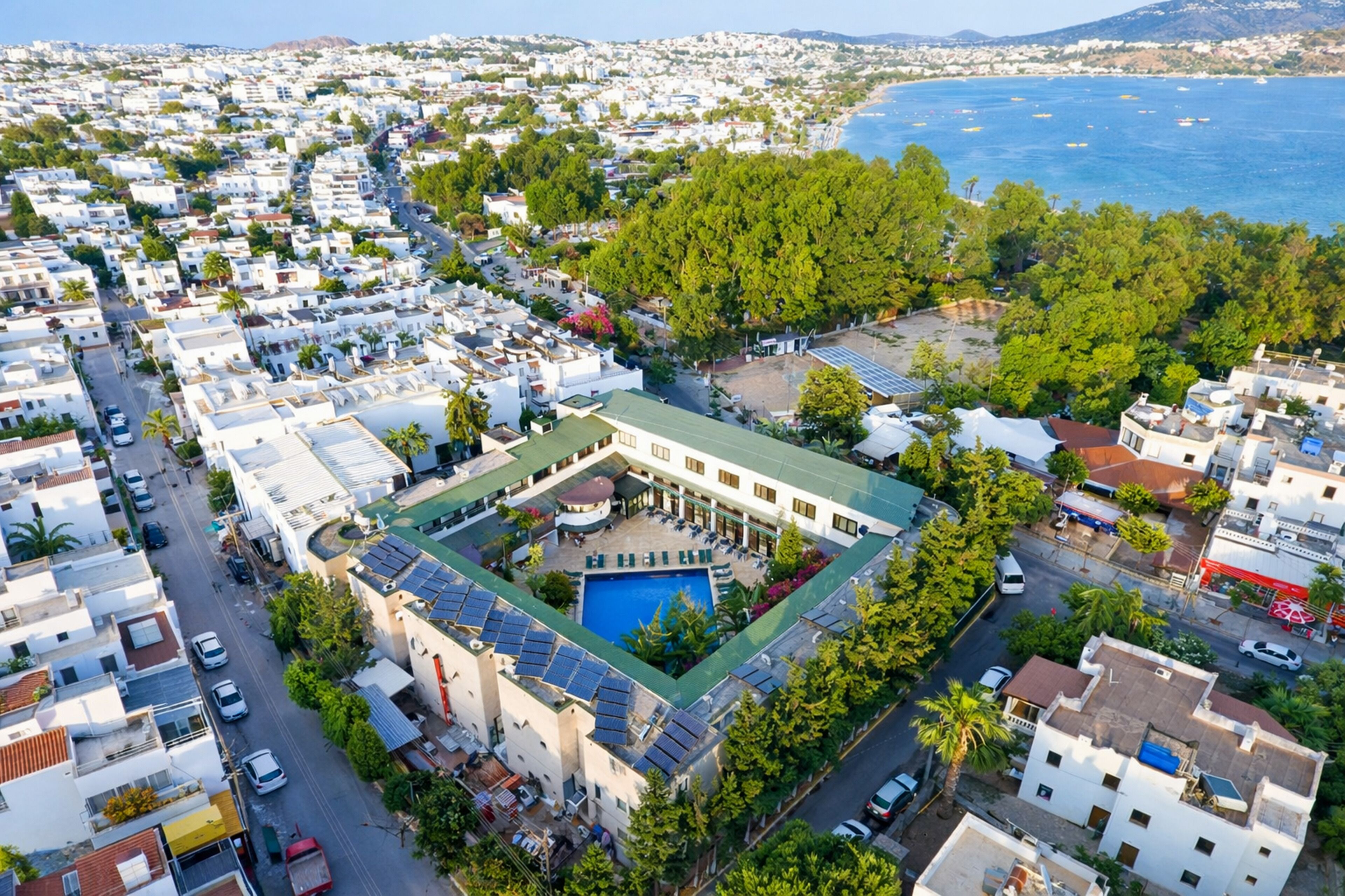 A coastal hotel with a swimming pool, solar panels, and a view of the sea.