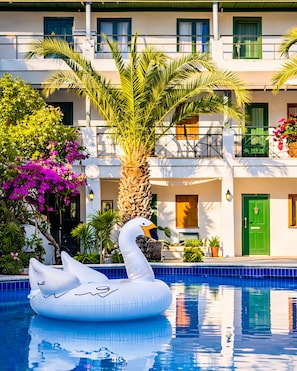 A swimming pool with a swan inflatable, palm trees, and a building with balconies. - Hotel Bleu Nuit Bodrum (Bodrum)