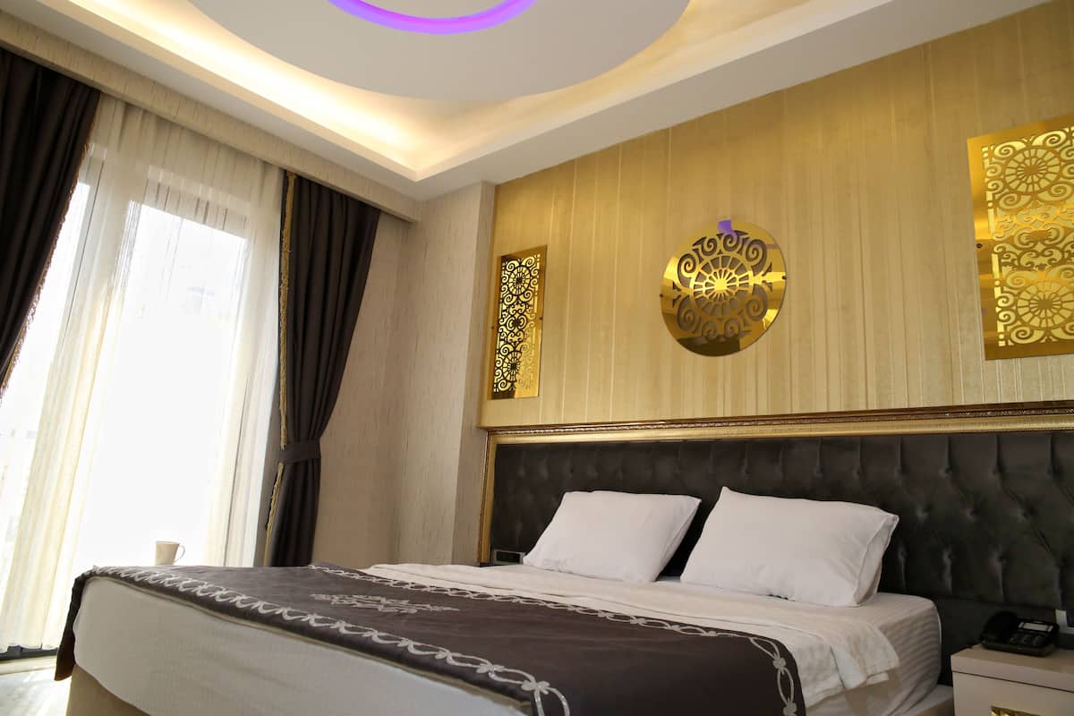 A hotel room with a large bed, a bedside table with a phone, and decorative wall panels.
