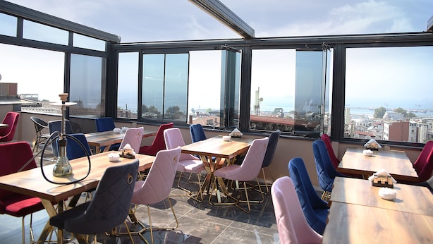 Zona de menjador a la terrassa amb taules i cadires, grans finestres i vista a la ciutat.