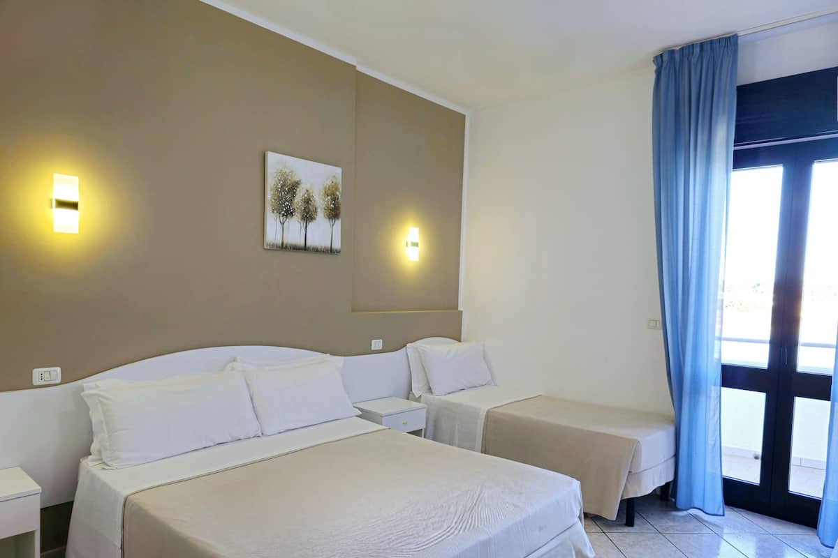 Ein Hotelzimmer mit einem großen Bett, zwei kleineren Betten, einem Nachttisch, einer Wandleuchte und einem fenster mit Vorhängen.