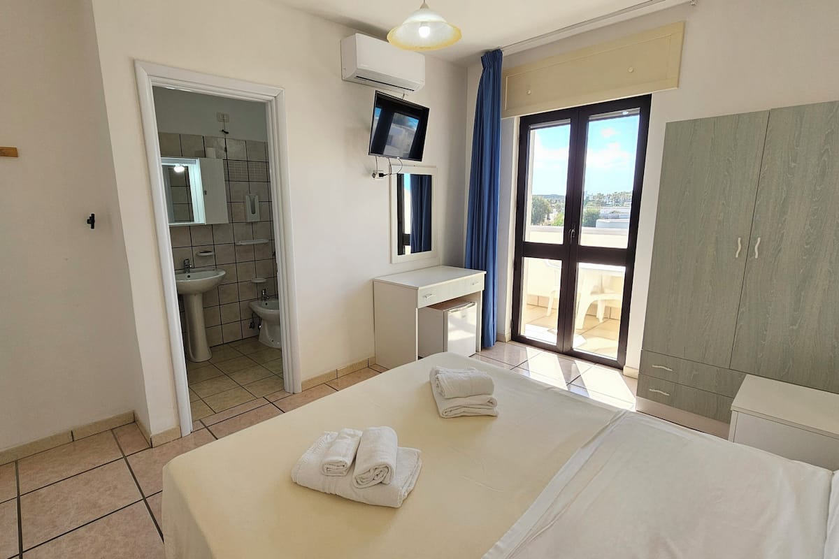 Ein Hotelzimmer mit Bett, Schreibtisch, Spiegel, Waschbecken und Kleiderschrank.