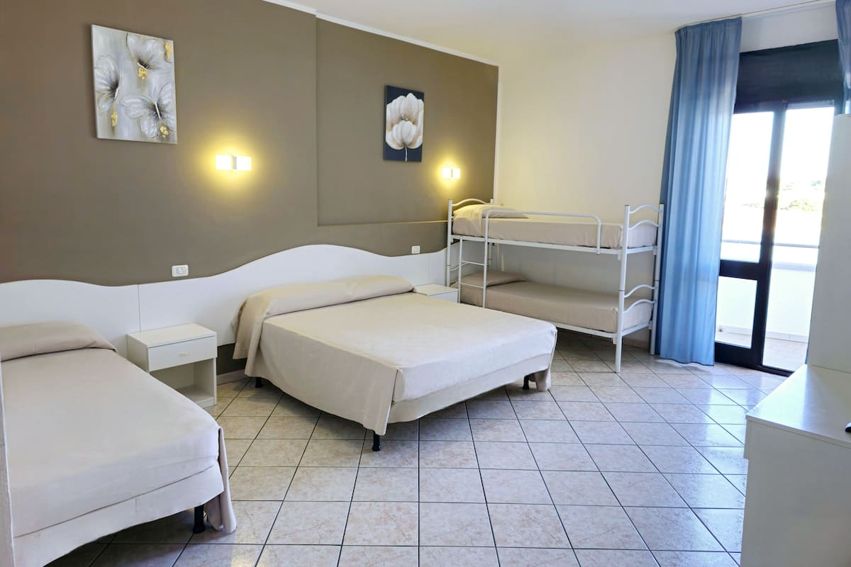Ein Hotelzimmer mit einem Etagenbett, einem Einzelbett, einem Nachttisch, einer Lampe und einem Bild an der Wand.