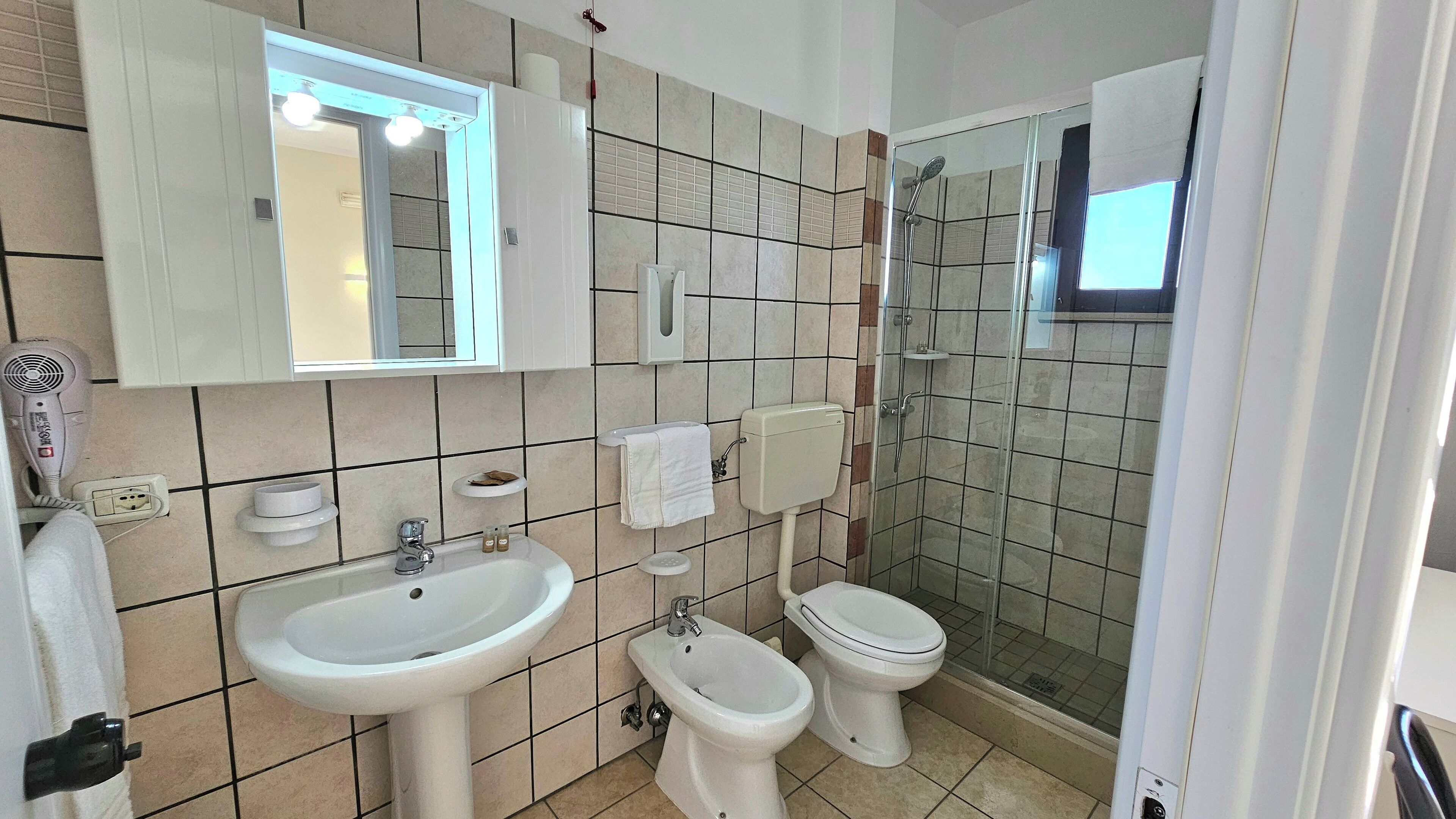 A bathroom with a sink, bidet, toilet, and a glass-enclosed shower.