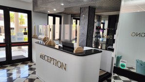 Ein Empfangsbereich mit Schachbrettmuster-Boden, einem Empfangstresen mit der Aufschrift "RECEPTION" und einer Glastür, die nach draußen führt.