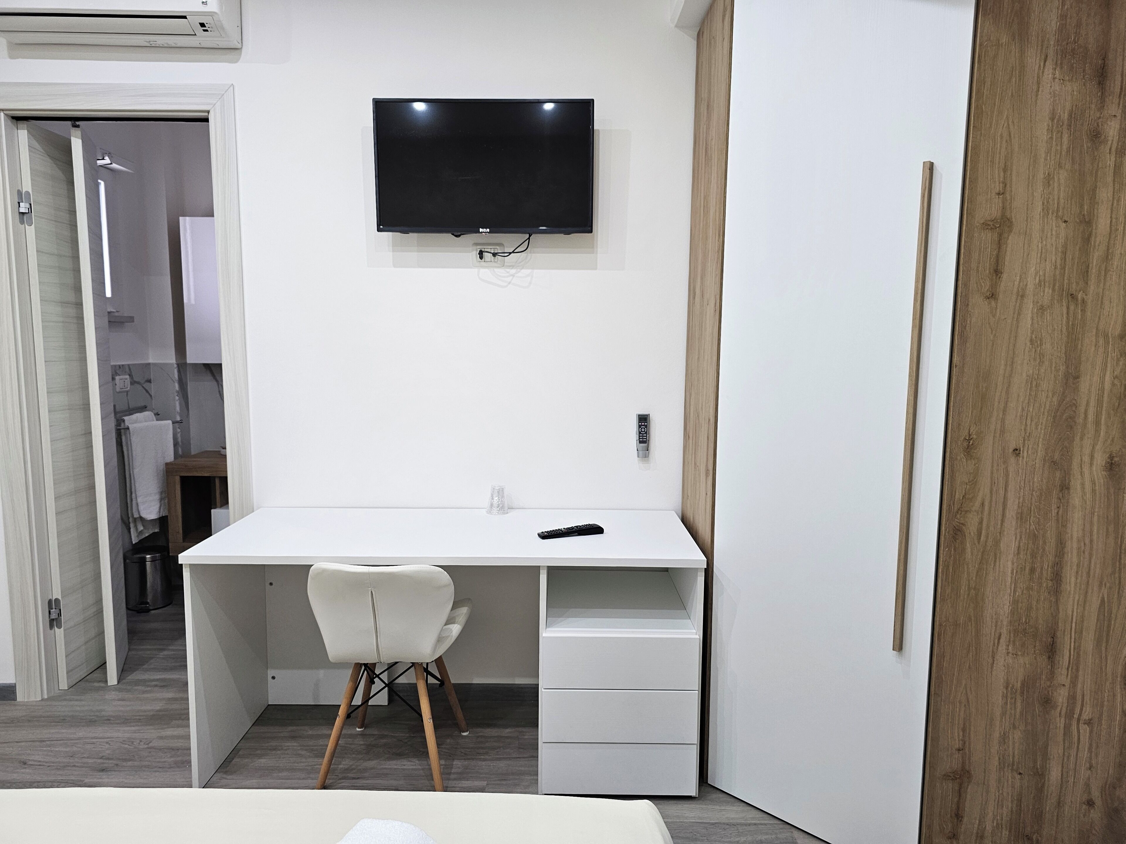 A modern bedroom with a white desk, a chair, a bed, and a TV mounted on the wall.