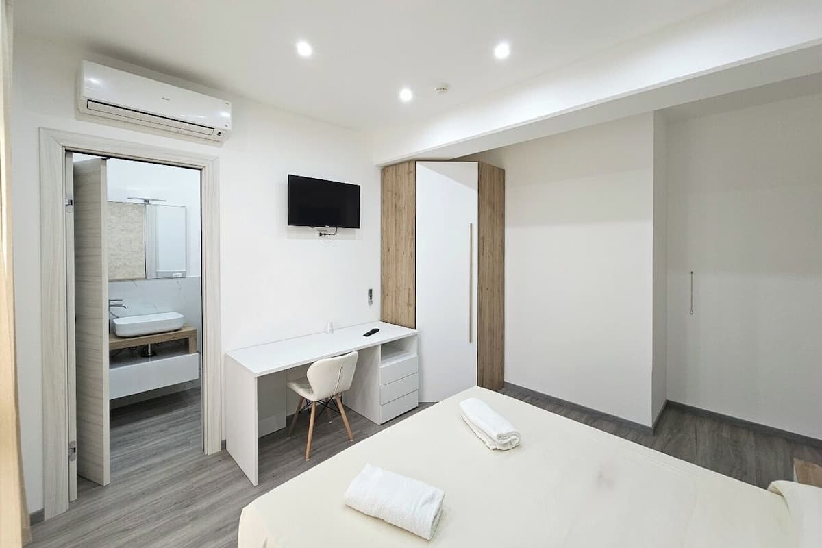 Ein modernes Hotelzimmer mit Bett, Schreibtisch, Stuhl, Fernseher und Kleiderschrank.