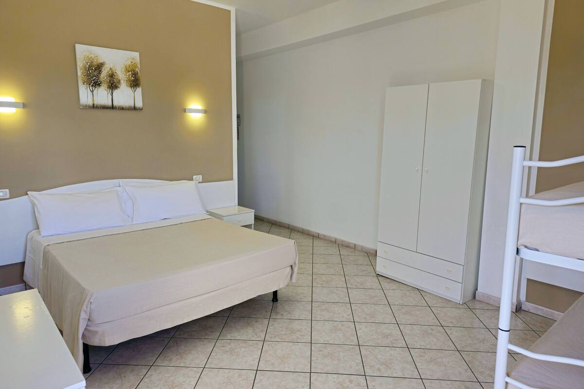 Ein Hotelzimmer mit Bett, Nachttischen, einem Kleiderschrank und einem an der Wand hängenden Kunstwerk.