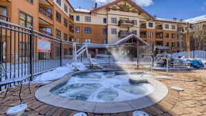 A spa area with a hot tub surrounded by a metal fence, a sign indicating spa rules, and a building with multiple balconies in the background. - Beautifully Updated 3 Bedroom in East Village - CS335 (Copper Mountain)
