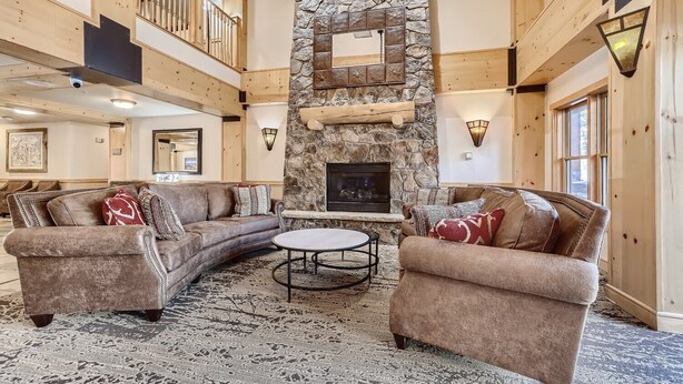 A spacious living area with a stone fireplace, wooden beams, and a high ceiling. - Beautifully Updated 3 Bedroom in East Village - CS335 (Copper Mountain)