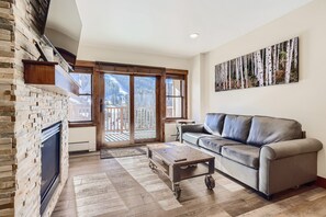 Un salon spacieux doté d’une cheminée, d’un canapé et d’une grande fenêtre offrant une vue sur une montagne enneigée.