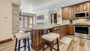 A modern kitchen with a central island, wooden cabinets, stainless steel appliances, and a stone accent wall. - Beautifully Updated 3 Bedroom in East Village - CS335 (Copper Mountain)