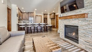 A modern living room with a fireplace, a kitchen with wooden cabinets, and a bar area. - Beautifully Updated 3 Bedroom in East Village - CS335 (Copper Mountain)