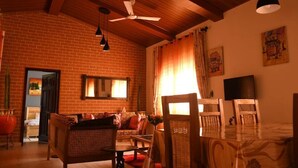 Un salón acogedor con pared de ladrillo, vigas de madera en el techo, un sofá, una mesa de comedor con sillas y ventiladores de techo.