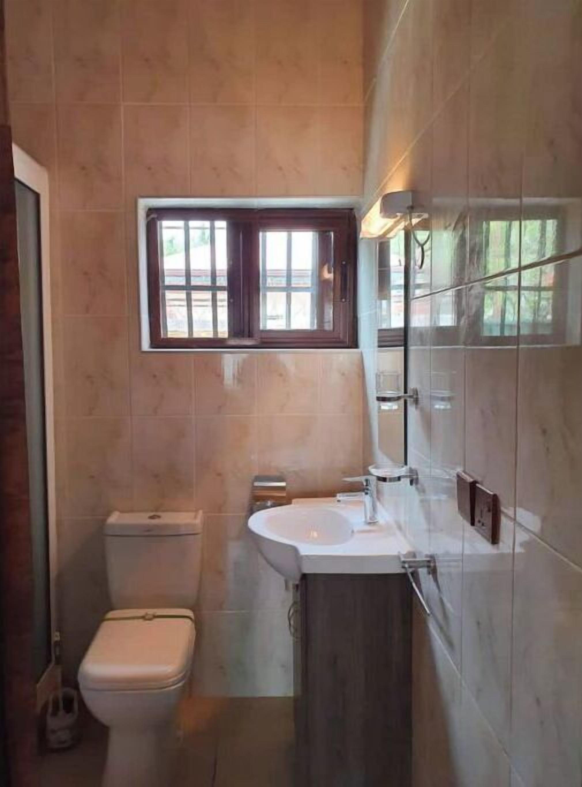A bathroom with a toilet, sink, and a window above the sink.