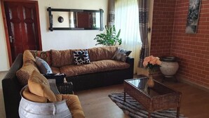 Una sala de estar con sofá, mesa de centro, sillón, planta en maceta y chimenea.