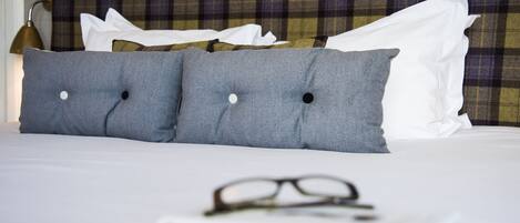 Una cama bien hecha con almohadas grises, un par de gafas y un cabecero escocés.