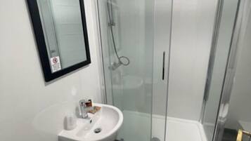 Un baño moderno con ducha de vidrio, lavamanos blanco y retrete.