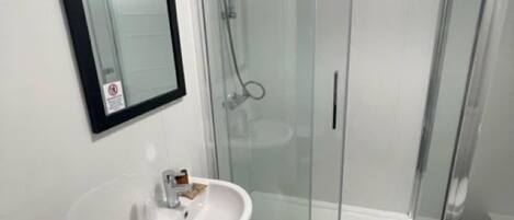 Un baño moderno con ducha de vidrio, lavamanos blanco y retrete.