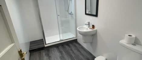 Un baño moderno con cabina de ducha de vidrio, lavabo blanco y retrete.