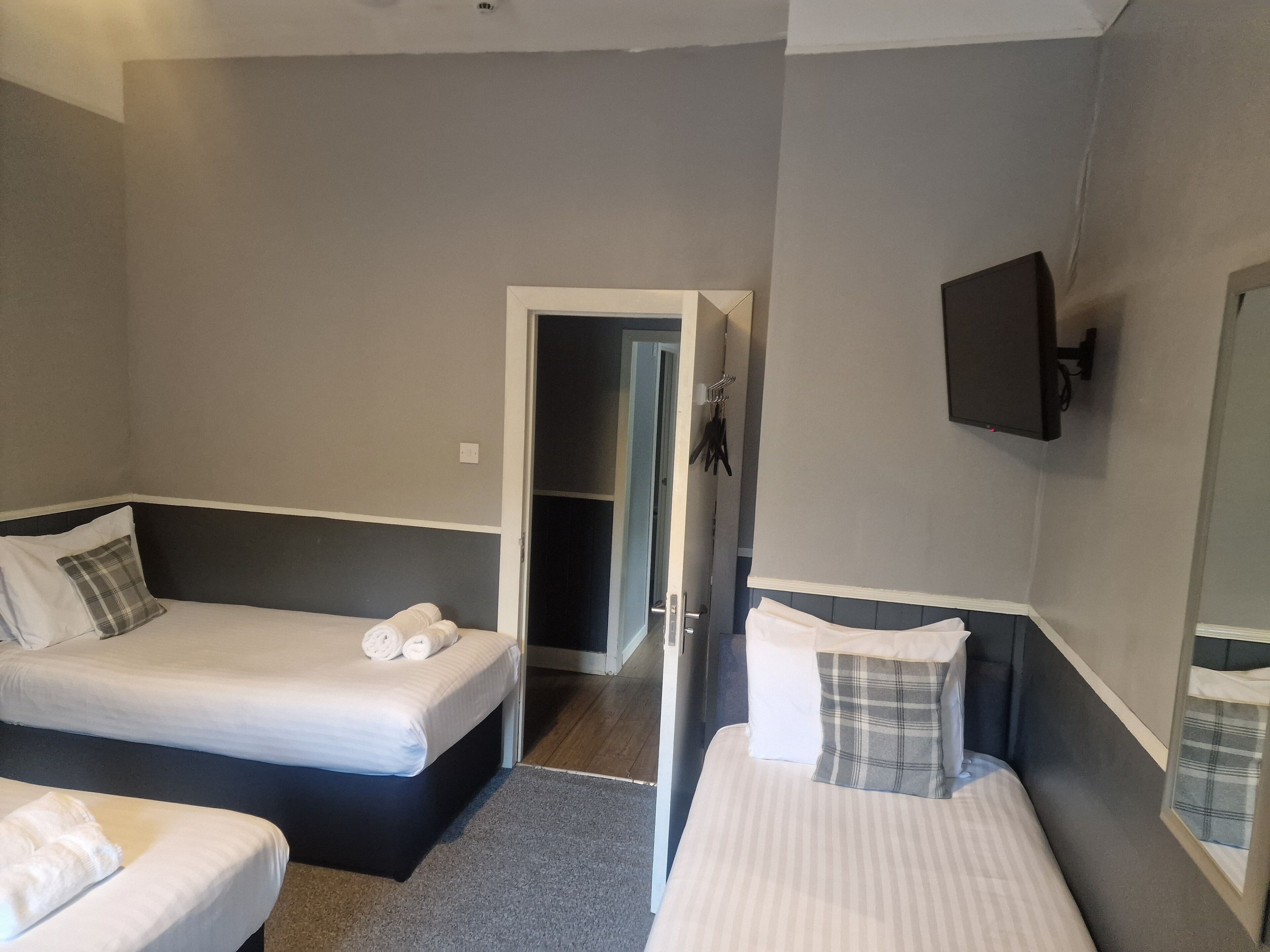 A hotel room with two beds, a TV mounted on the wall, and a door leading to a hallway.