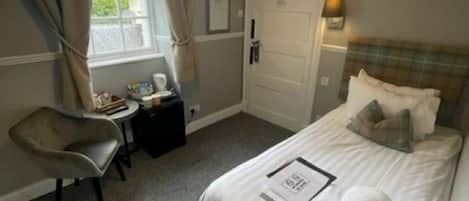 A hotel room with a bed, a desk, a chair, a window with curtains, and a door.
