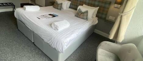 A hotel room with a large bed, a chair, a small table, and a wall-mounted lamp.