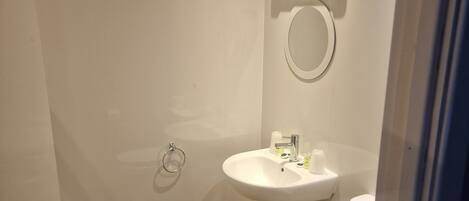 A small, modern bathroom with a wooden floor, white walls, a round mirror, a sink, and a toilet.