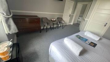 A hotel room with a bed, a dresser, two chairs, a television, and a small table with a tray of food.