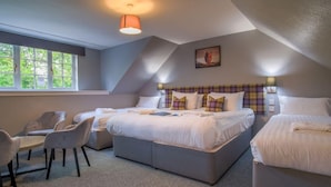 A bedroom with two beds, a desk, and chairs. There is a window providing natural light, and a painting on the wall. - Isle of Skye Guest house (Kyleakin)