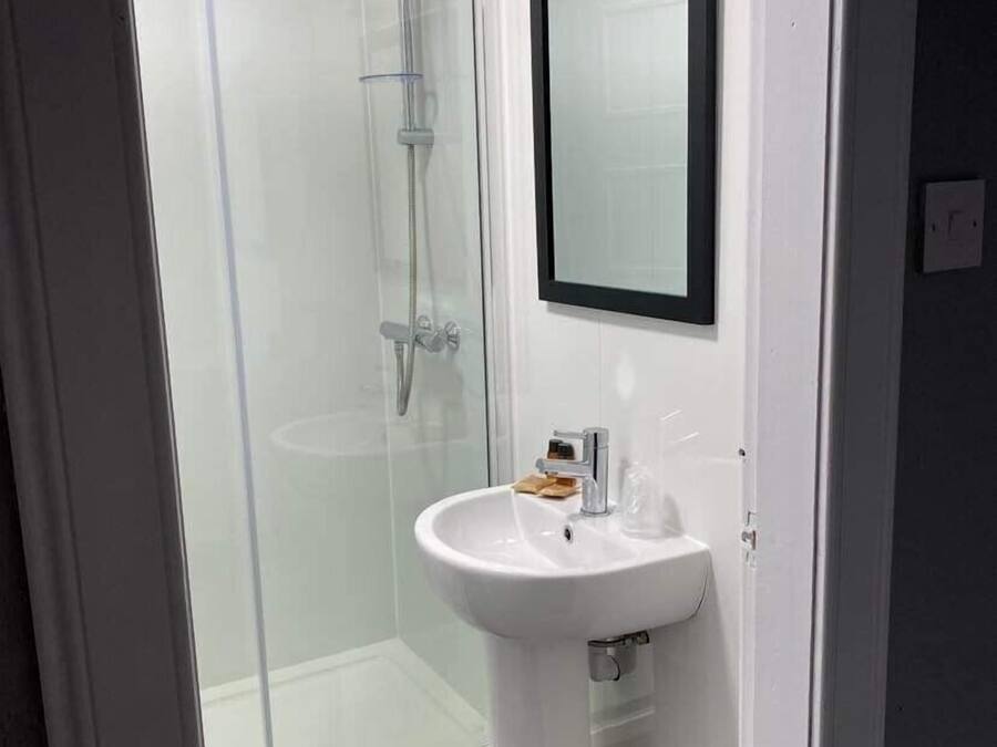 Un baño moderno con cabina de ducha de vidrio, un lavabo blanco y un espejo.