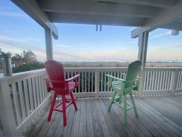 A covered porch with two Adirondack chairs facing a view of the beach.