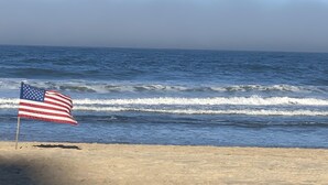 Ein Strand mit einer amerikanischen Flagge auf einem Fahnenmast, Wellen im Meer und einem klaren Himmel.