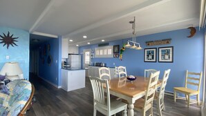Ein Essbereich mit Holztisch und weißen Stühlen, eine Küche mit weißen Schränken und blauen Wänden.