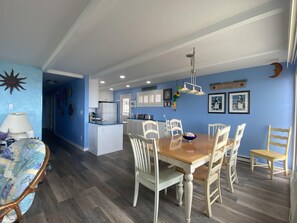 A dining area with a wooden table and white chairs, a kitchen with white cabinets, and blue walls.