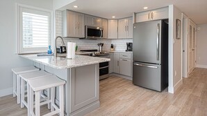 Una cocina moderna con armarios grises, electrodomésticos de acero inoxidable y una isla central con taburetes de bar.