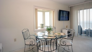 A dining area with a glass table, metal chairs, a potted plant, and a television on the wall. - Enjoy the beautiful view of the Ocean from this one bedroom condo located in midtown! (Ocean City)