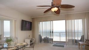 A spacious living area with a glass table, chairs, a ceiling fan, and a view of the ocean through large windows. - Enjoy the beautiful view of the Ocean from this one bedroom condo located in midtown! (Ocean City)