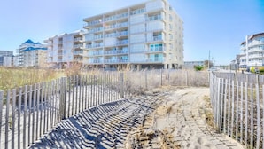 A multi-story hotel with balconies, a sandy pathway, and a wooden fence. - Enjoy the beautiful view of the Ocean from this one bedroom condo located in midtown! (Ocean City)