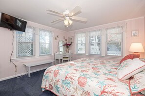 Une chambre à coucher comprenant un lit, un bureau, une chaise, un ventilateur de plafond et un téléviseur fixé au mur.